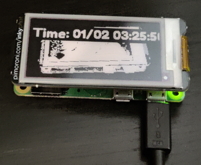 The Inky pHAT showing a photo of itself with the current time printed on top of it